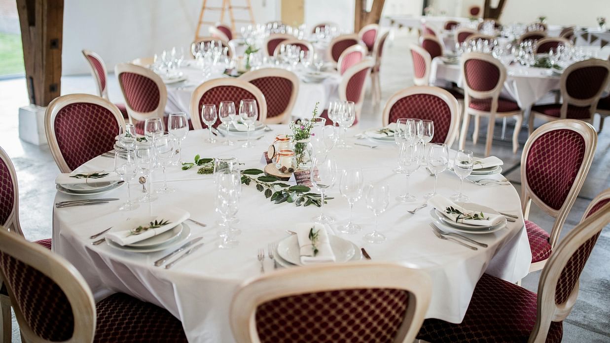 a round table with maroon coloured cushioned chairs and well set cutlery and glassware
