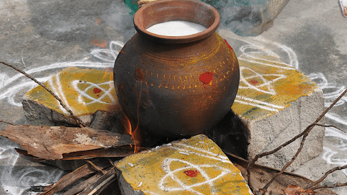 A brass pot on fire with boiling milk and surrounded by rangoli