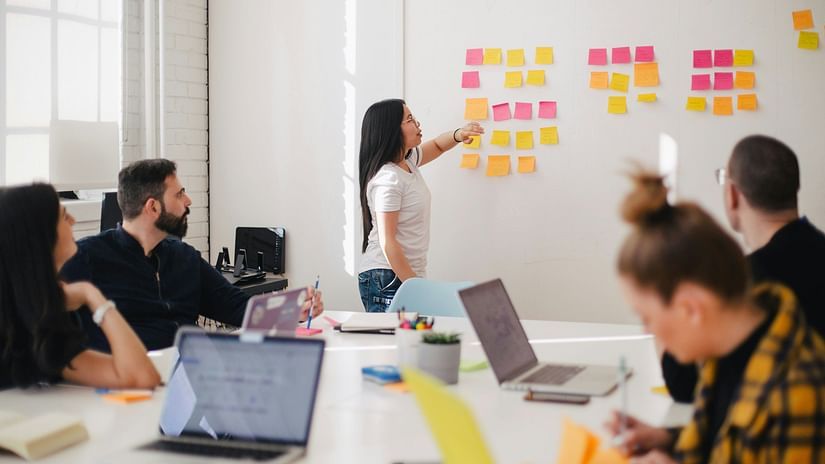 A meeting room with a speaker turned towards a board filled with sticky notes