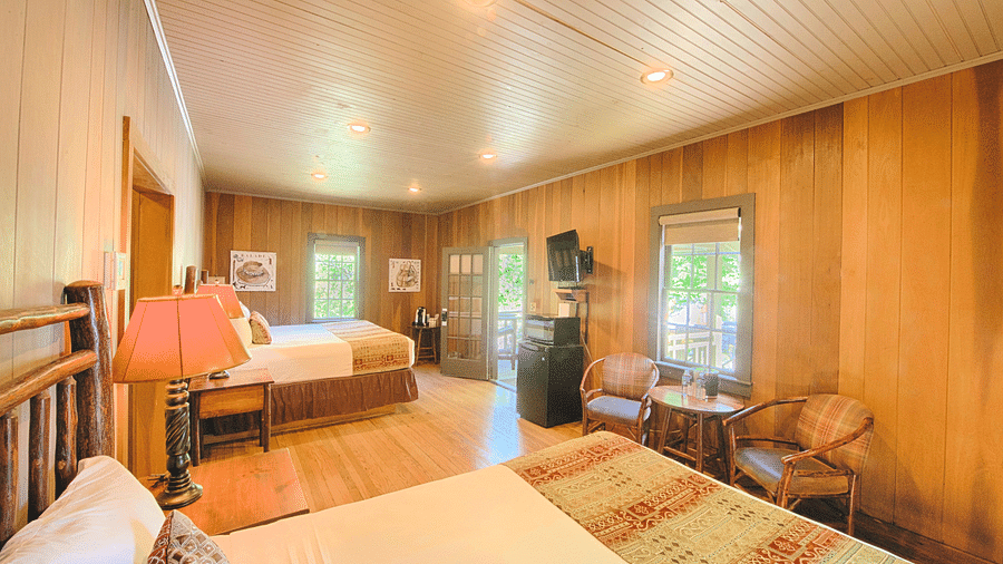 corner view image of a bedroom featuring two plush double beds with a coffee table in front of it - Historic Tapoco Lodge