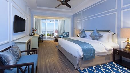 Twin beds with a side balcony view and a wall-mounted TV opposite the bed