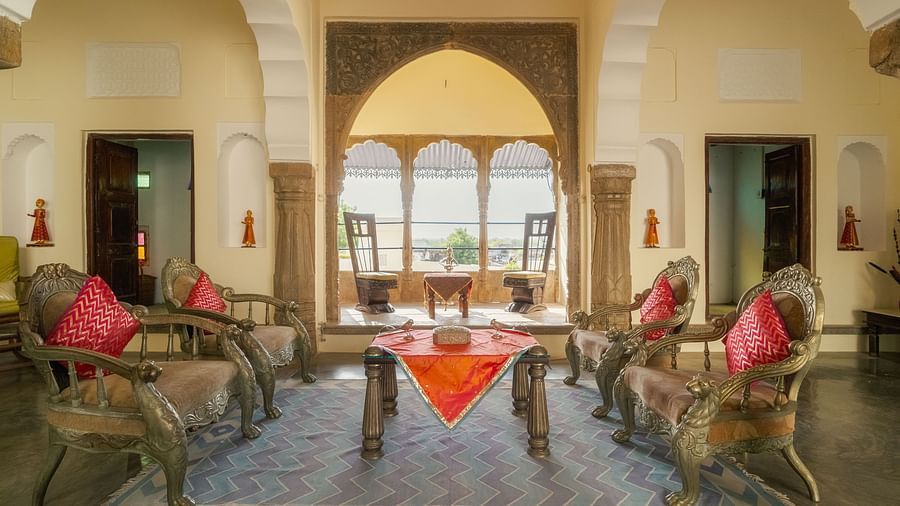 A richly decorated hallway at Fort Barli, illuminated with warm light, leads towards a grand wooden door.