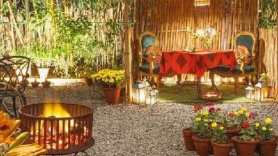 Outdoor dining setup at Karma Chalets with wooden benches, string lights, and a food counter in a garden setting.