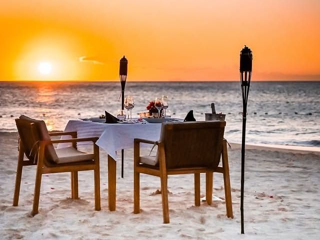 Dining setup with tables and chairs on the beach during sunset at Tamarind Hills Resort and Villas - Antigua.