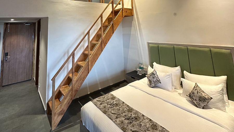 A spacious hotel room with a king-size bed, a wooden ceiling, and a loft area accessible by a staircase.