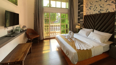 Sunlit premium room featuring a wall-mounted TV, decorative stone wall accents, and luxury bedding - DAN Resorts & Weddings, Palghar