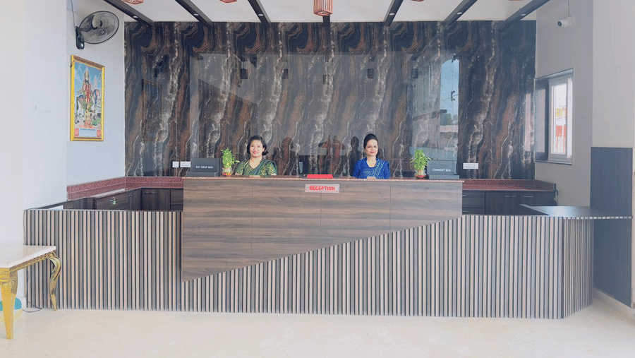 A reception desk with a striped front and wooden beams above is attended by staff - Kankidham Lords Inn