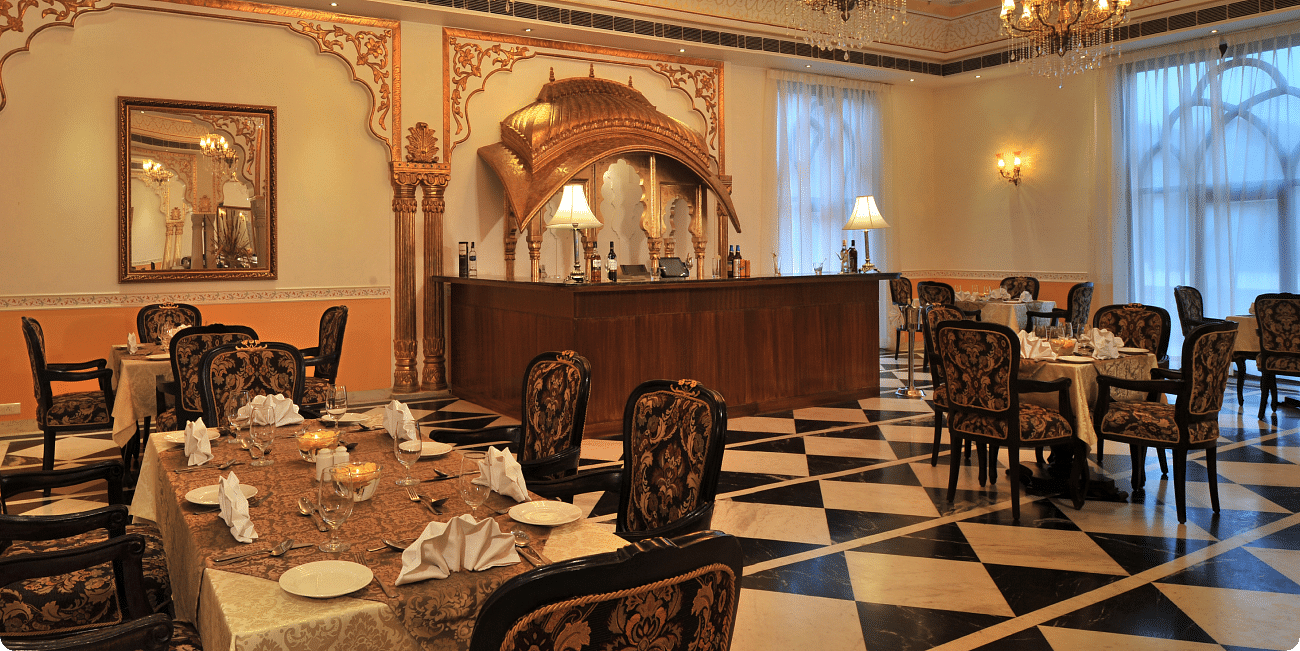 Dining area at Rajasthali Resort & Spa Jaipur with chairs, tables and chandeliers hanging from the ceiling.