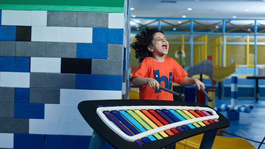 An expressive young boy enthusiastically plays a large, colourful outdoor-style xylophone in a music play zone at Tic Tac Tot.
