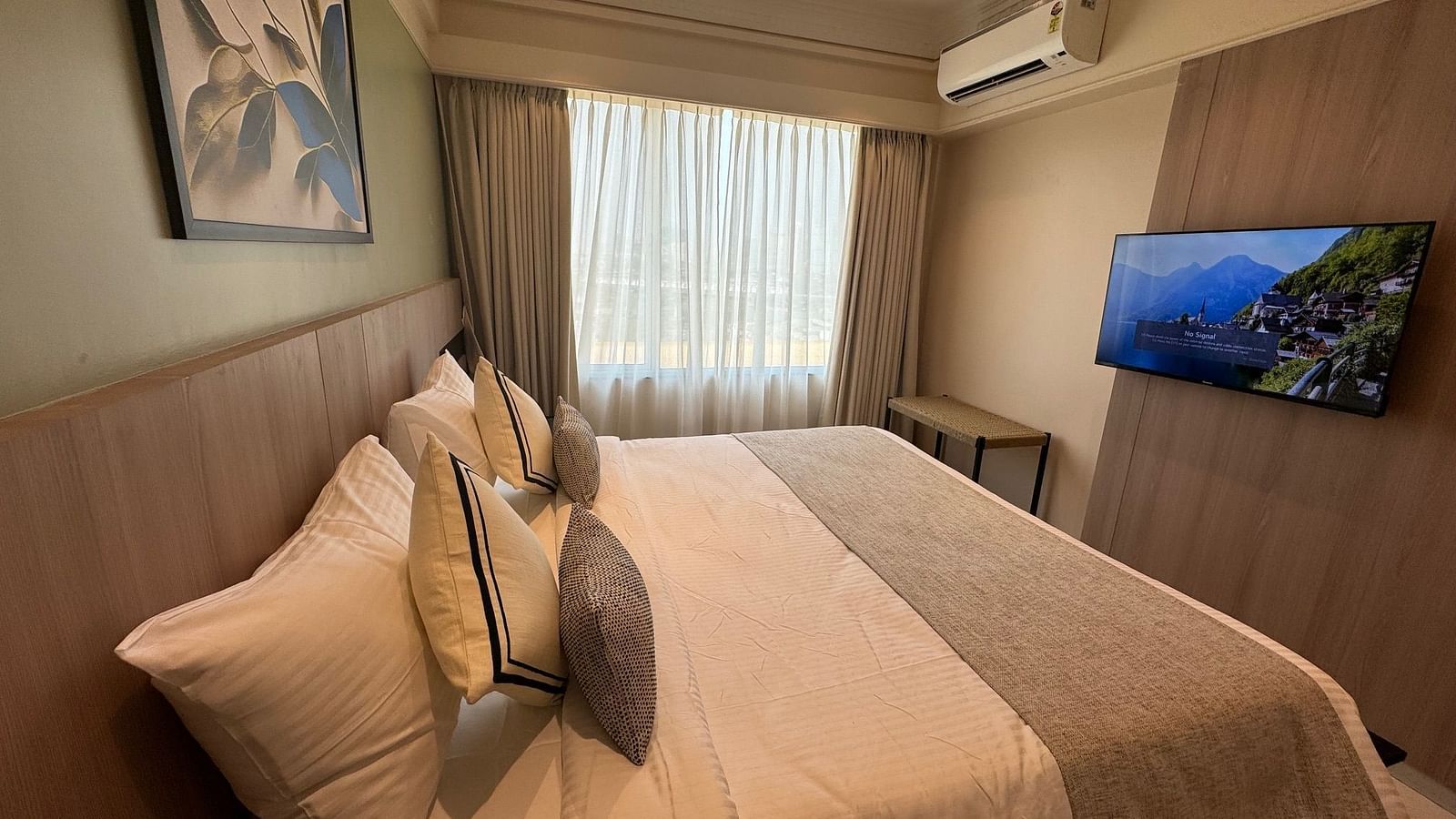 A king bed with a tv opposite it and a paiting hung above it in deluxe room - Hotel Mumbai House, Valnai, Malad