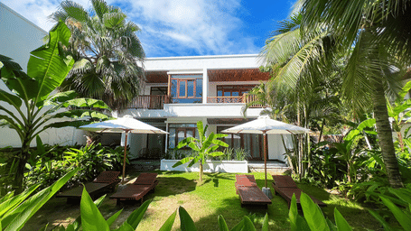 A facade view of Alibu Resort Nha Thrang - A Waterfront Wedding Venue, with trees and a manicured garden in the foreground.