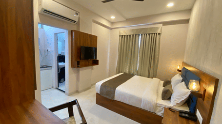 A room at Hotels Mumbai House with a large bed, bedsheets, pillows, a television, a fan,  and an air-conditioner.