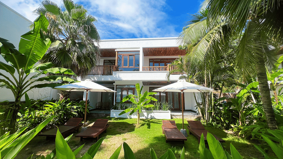 Facade of Alibu Resort Nha Trang featuring a lush tropical garden with a serene outdoor seating area and coastal greenery.