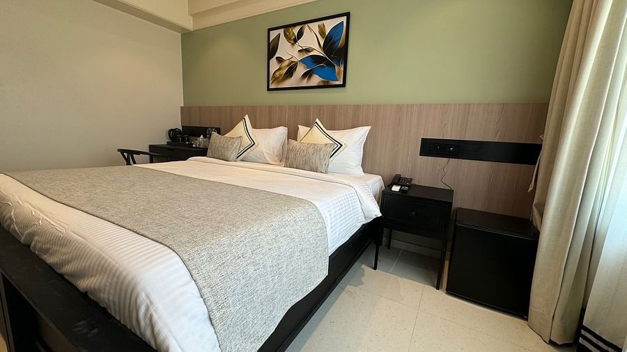 Side view of the king bed with a painting hung above and a side table next to it inside deluxe room - Hotel Mumbai House, Valnai, Malad