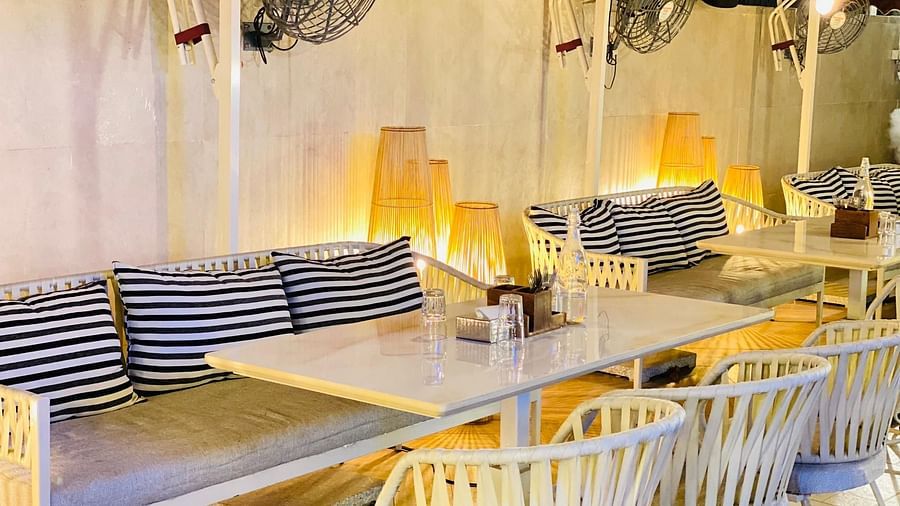 Indoor dining area with white chairs, wooden tables, and striped cushions at Hotel Mumbai House Mindspace, Malad.