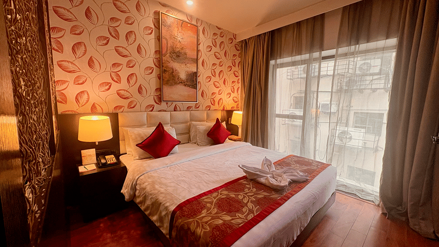 An inclusive shot of the spacious bedroom in the well-lit Executive Suite at Senses Hotel with a King-size bed, bedside tables and a curtained long glass window.