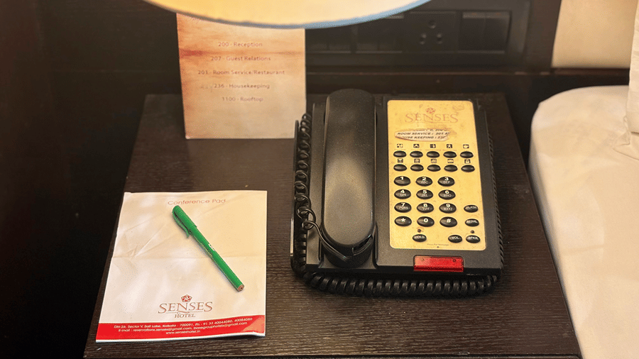 Intercom dial phone with relative phone numbers and a conference pad with a pen placed on the bedside table at a Senses Hotel room.