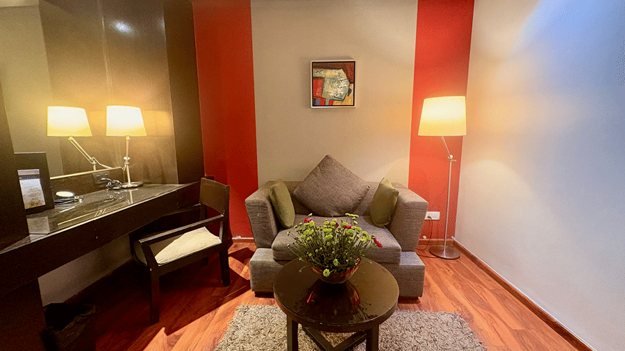 Front view of a cushioned sofa with a centre table and mirrored work desk in the well-lit sitting area of the Executive Suites at Senses Hotel.