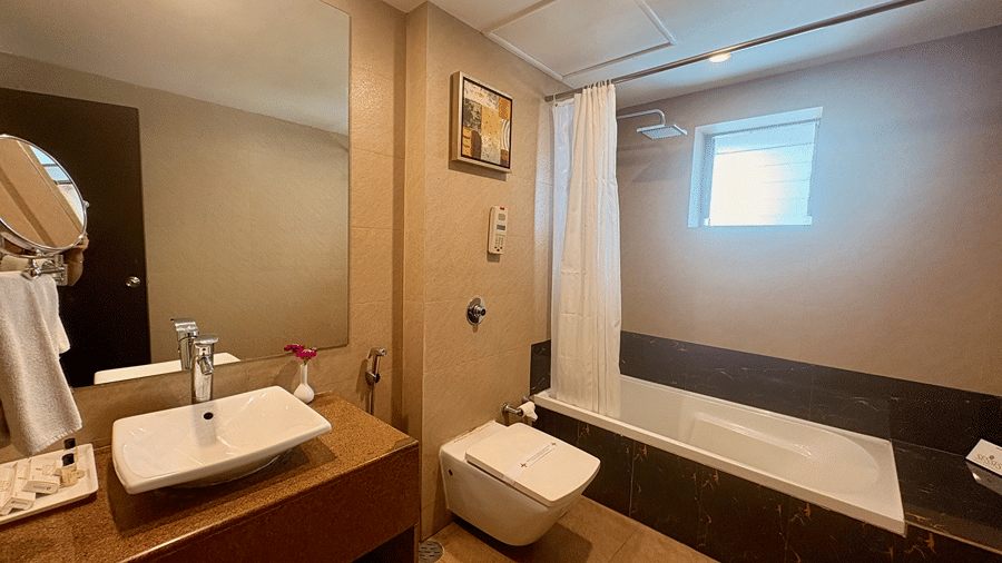 The bathroom in the Executive Suite at Senses Hotel featuring a sink with a large wall-mounted mirror, a western commode with a faucet and a curtained shower area with a bathtub.