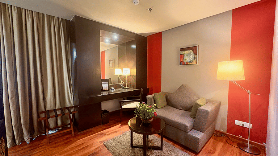Extended view of the separate sitting area of the Executive Suite in Senses Hotel featuring a cushioned sofa, a well-lit work desk and curtained windows.