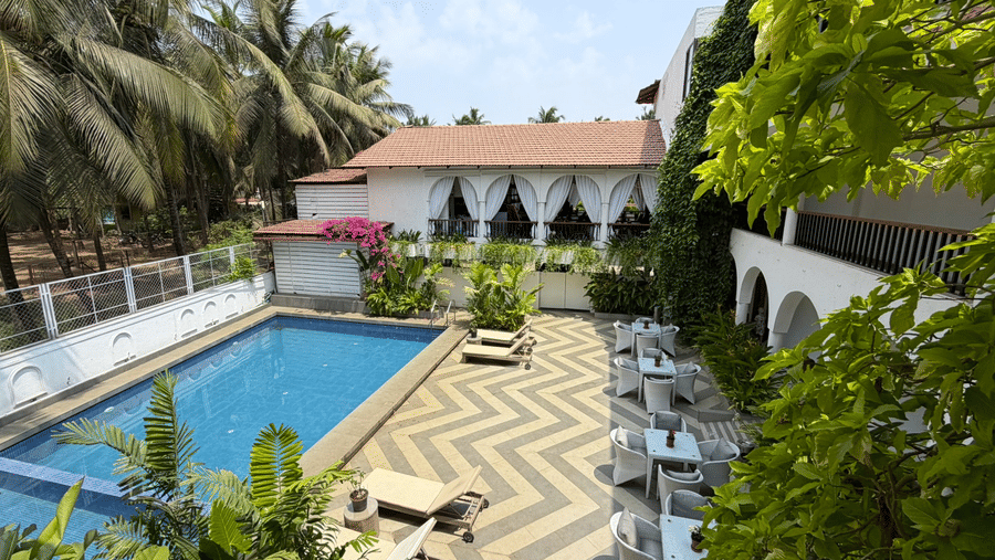 A high angle shot showing a swimming pool, outdoor dining furniture, surrounding palm trees at Bougainvillea, Alibaug.