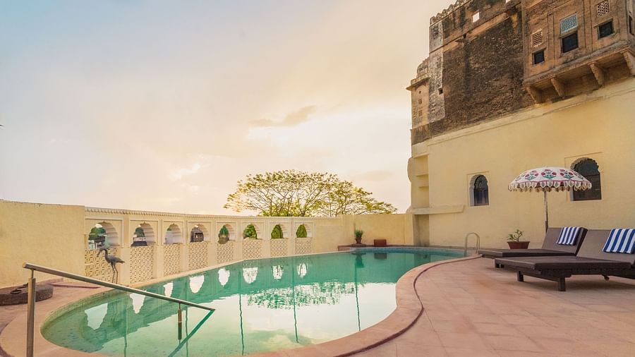 A tranquil pool at Fort Barli, flanked by historic walls and lounge chairs, offers a serene escape with a touch of grandeur.