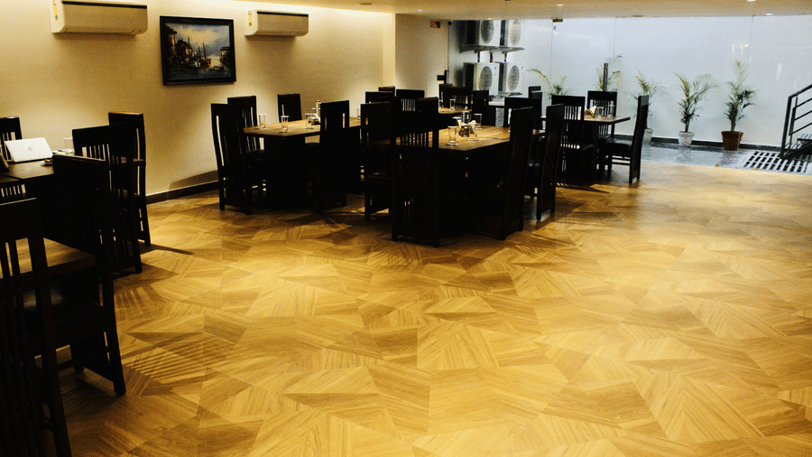 A brightly lit dining hall showcasing a clean open-plan layout with dark wooden furniture and potted plants - Hotel 91 HUDA City Centre, Gurugram