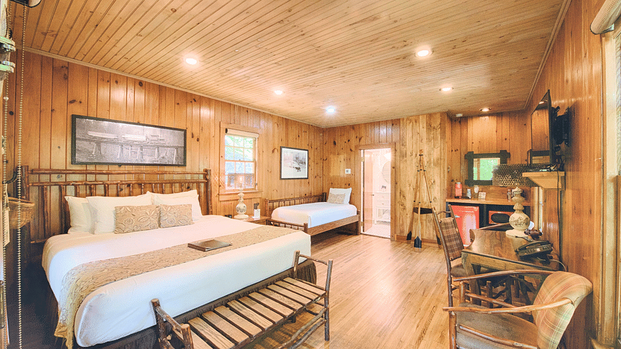 full view image of a the mountain view room with cozy wooden interiors along with a comfortable double bed with a wide landscape portrait above its headboard - Historic Tapoco Lodge