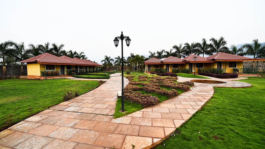 A stone pathway winds through a lush green lawn, leading to a row of Deluxe Cottages at The Kanila Resort.