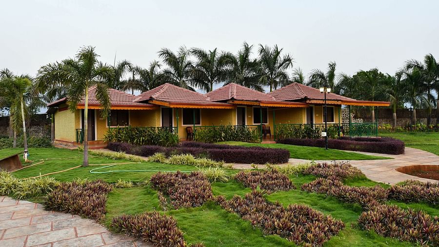 Facade of Deluxe Cottage at the Kanila Resort featuring a lush green lawn with a pathway and trees. 