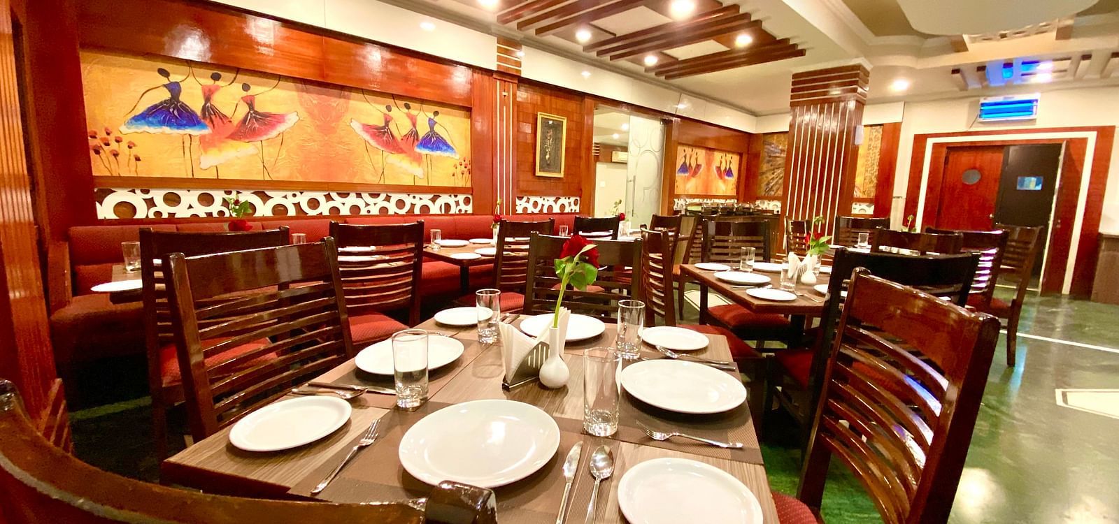 Dining area at DLS Park Grace, Haridwar featuring wooden chairs, ceramic plates, wall art and false ceiling.