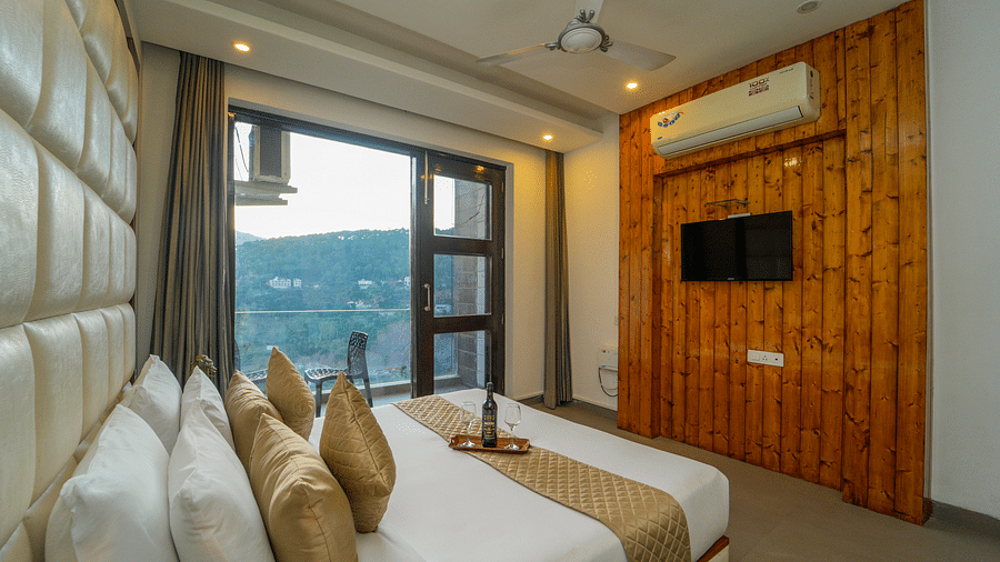 An image of the premium room with a bed, flat screen TV, and a glass door leading to the balcony overlooking the view - DLS Whispering Winds