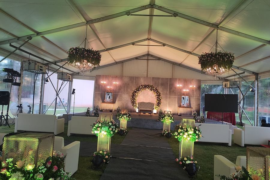 A beautifully decorated event tent with green floral arrangements, elegant lighting, and a stage set for a formal occasion or wedding ceremony - Black Thunder, Coimbatore