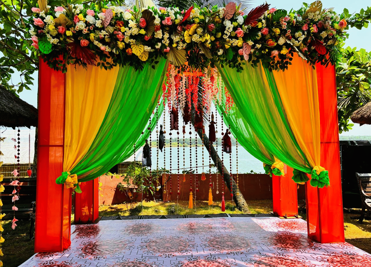 Wedding mandap decorated with orange and green drapes, flowers, and hanging garlands at Paradise Lagoon Resort, Udupi.