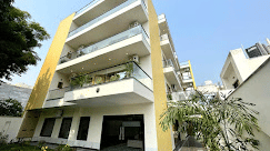 White multiple storey building exterior of Lime Tree Hotels & Service Apartment Private Limited featuring balconies on each floor, surrounding trees, and a clear sky.