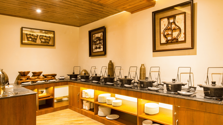 The buffet counter at The Pine Grove Fine-dining Restaurant featuring multiple covered serving pots, wooden cabinetry, and neatly stacked plates | Mount Lungta Boutique Hotel & Spa