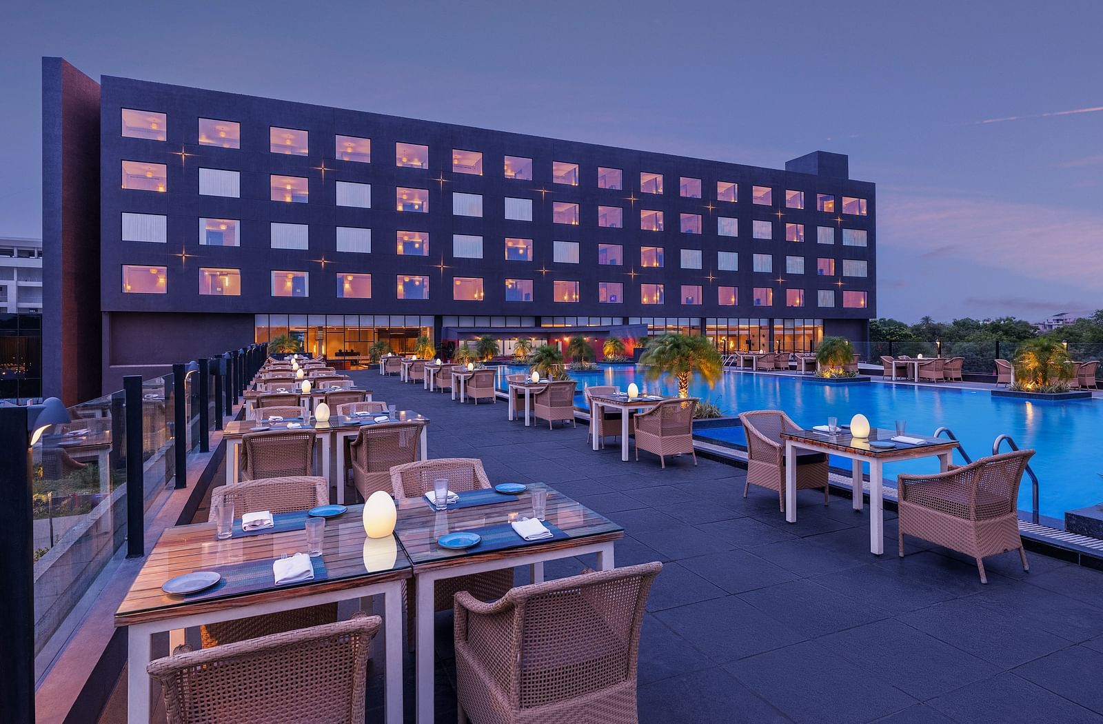 Poolside seating arrangement with the Essentia Luxury Hotel, Indore building in the backdrop.