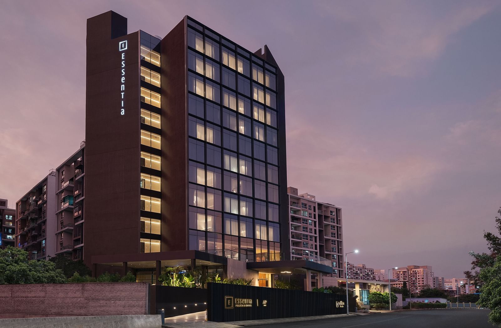 Facade of Essentia Premiere, Pune with lights on during twilight.