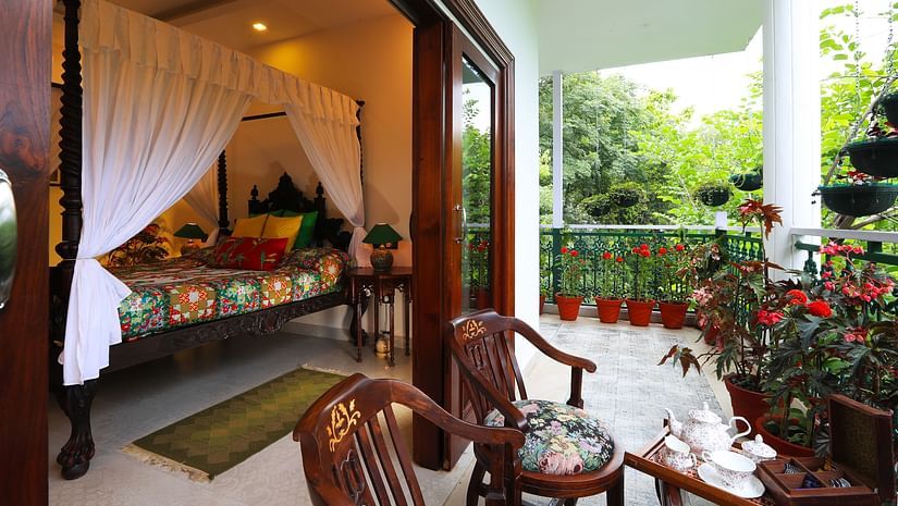 Bedroom with a four-poster bed, balcony, and a view of lush greenery.