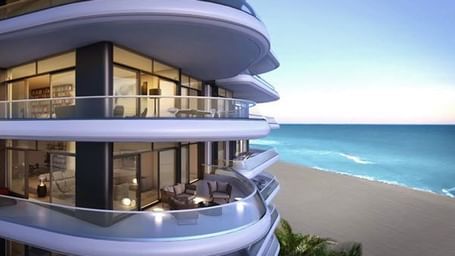 The exterior view of a multi-storey curved building with balconies facing the sea and the beach below.