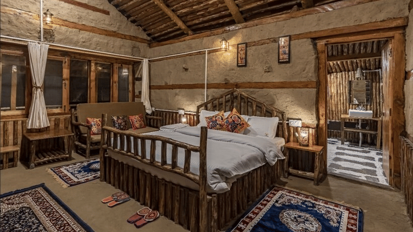 Close-up shot of a double bed with a wooden bed frame alongside a door leading towards the bathroom at Amara Upepo - The Sky Village, Manali.