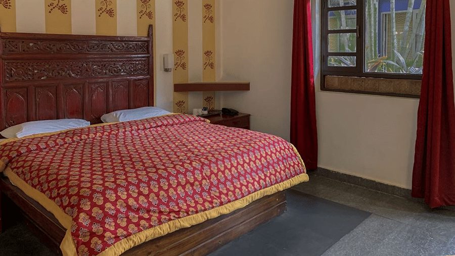 Bedroom with a double bed, red patterned bedding, carved wooden headboard and a window overlooking the surroundings.