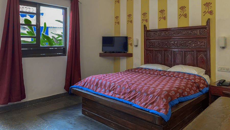 Bedroom with a double bed featuring red patterned bedding, wooden headboard, curtains and a wall-mounted television.