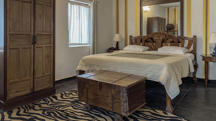 King size bed with white bedding, wooden furnishings, striped walls and a window bringing in natural light.