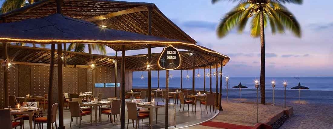 A beach shack with a coconut tree next to it at Caravela Beach Resort, Goa - restaurants in South Goa