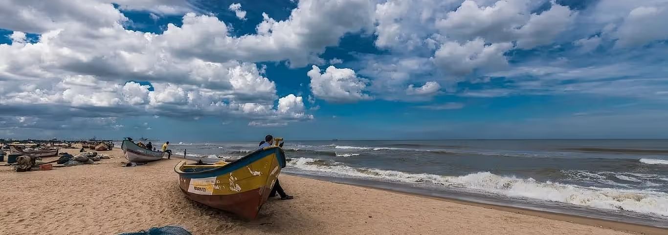 A fishing boat rests on a sandy beach as waves meet the shore under a dramatic, cloud-filled sky