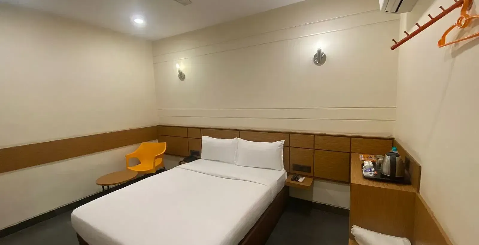 View of a hotel room with a single bed, wooden accents, and warm lighting - Max Hotel Prayagraj.
