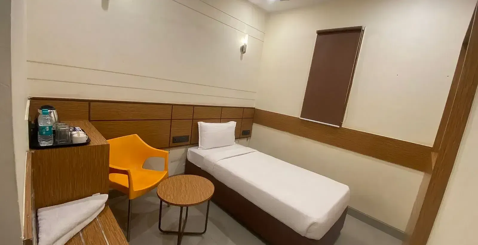 View of a hotel room with a single bed, wooden accents, and warm lighting - Max Hotel Prayagraj
