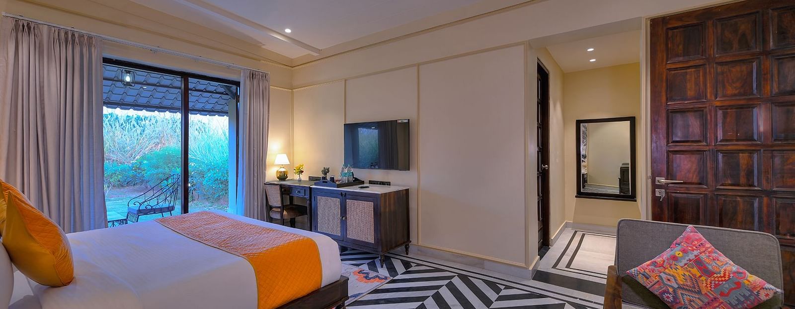 Superior Cottage with a bed featuring orange accents, black and white chevron flooring, a seating chair with a patterned pillow, a work desk, and a view to the outside - Singhvilas, Ranthambore