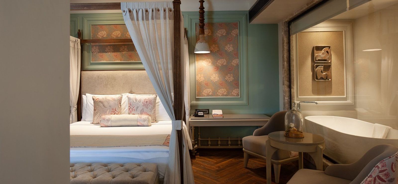 A serene corner of a suite at The Evren, Vagator, showing the four-poster bed and a glimpse of the luxurious bathroom with a freestanding bathtub visible through a glass partition.